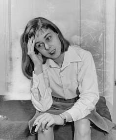 Photo en noir et blanc d’une jeune femme assise sur un perron, la tête appuyée sur une main tandis qu’elle tient une cigarette dans l’autre