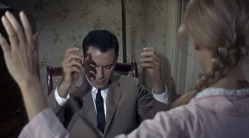 Photo tirée d’un film montrant un homme assis en costume, les yeux fermés, la tête baissée et les mains levées