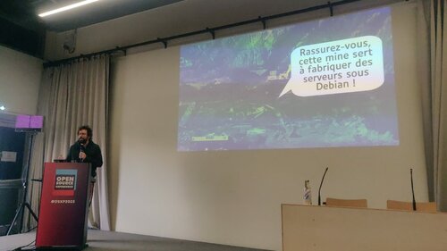 Une photo de la conf, avec une slide qui montre une mine en Afrique, et une bulle qui dit : « Rassuez-vous, cette mine sert à favriquer des serveurs sous Debian ! »