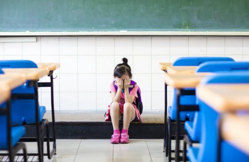 Une petite fille seule dans une salle de classe, la tête dans les mains